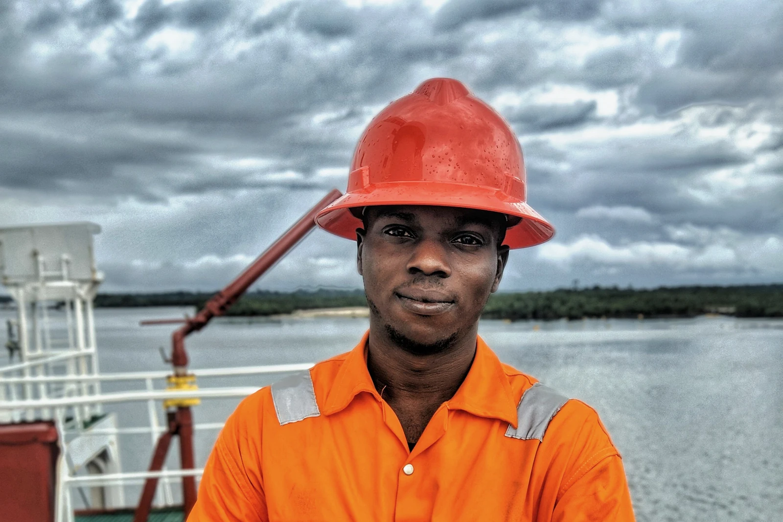 A deckhand in orange PPE and a hard hat on a ship's deck