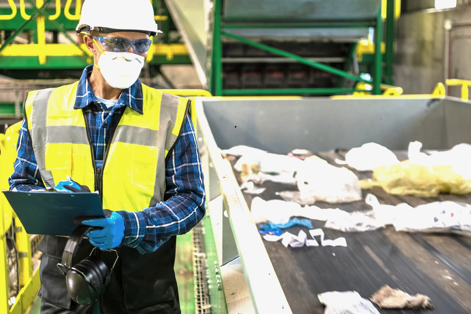 A recycling sorter in hi-vis, hard hat and respirator checking material on the sorting line