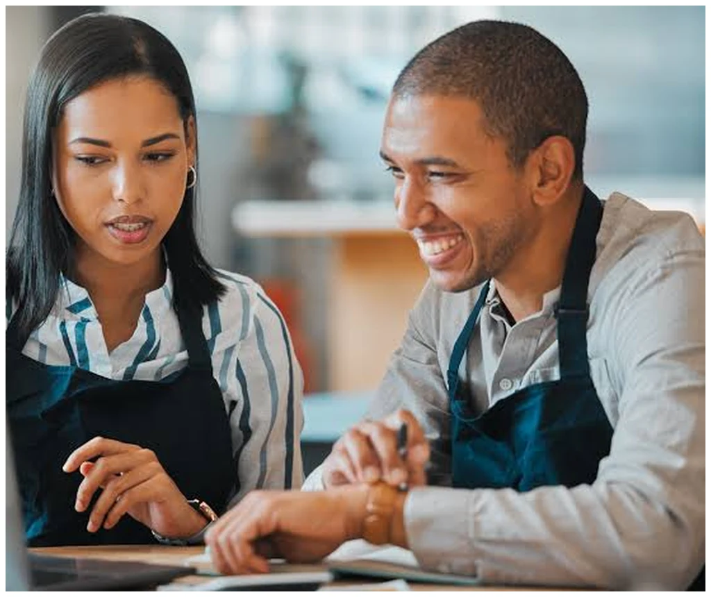 Two cafe staff reviewing performance and goals on a laptop