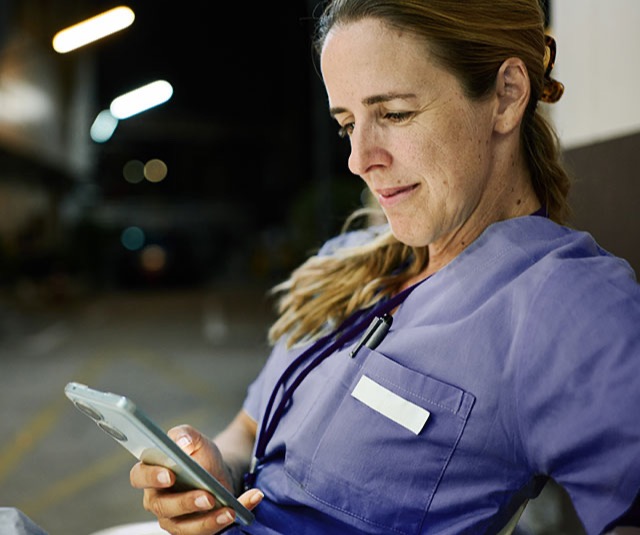 Healthcare worker in scrubs completing shift tasks on her phone