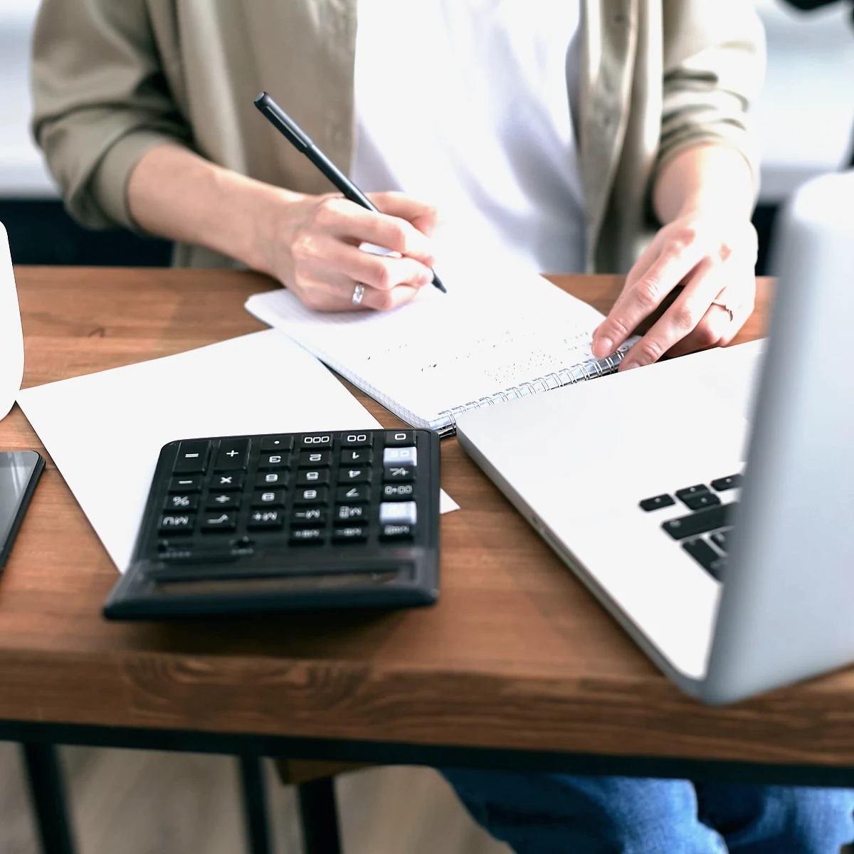 A bookkeeper working remotely, with a laptop, calculator and ledger