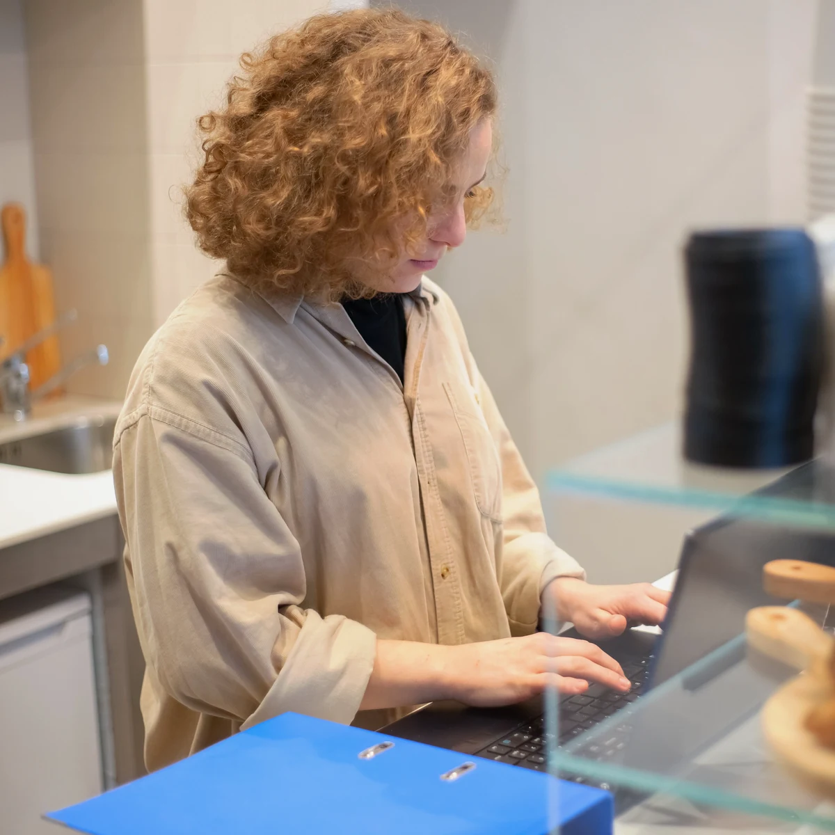 A coastal small-business owner doing the books on a laptop behind the counter