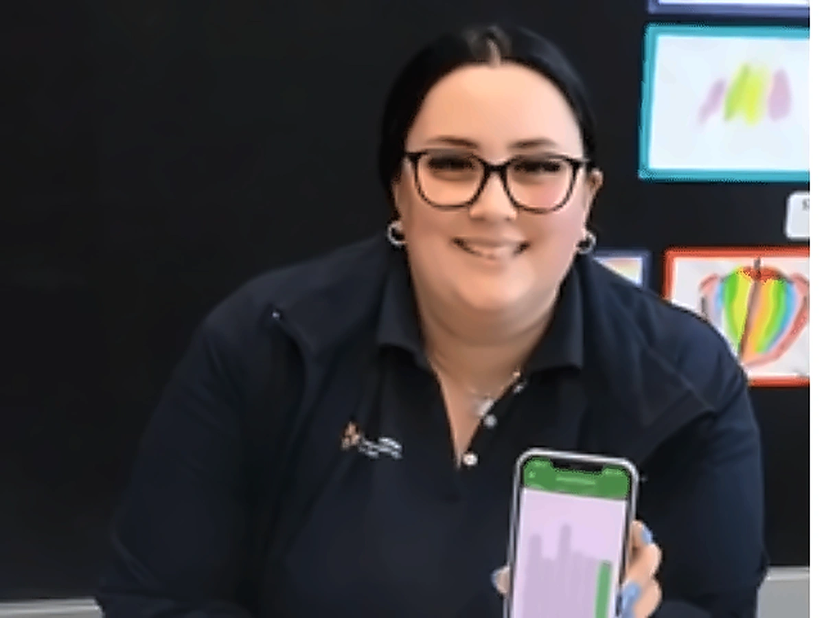 A smiling Toowoomba Catholic Kindergartens educator holding up the RosterElf app on her phone